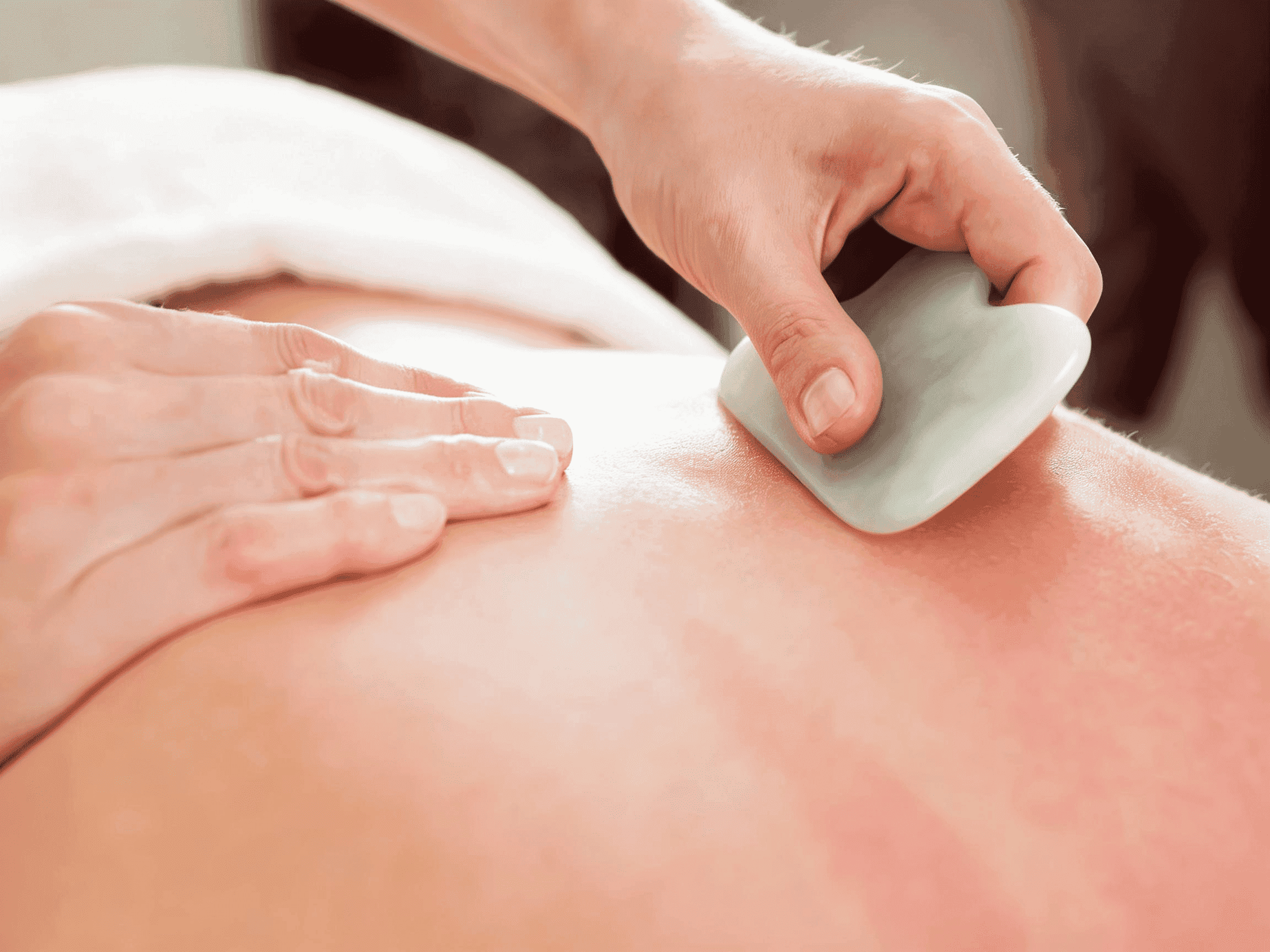 A jade gua sha tool resting on a linen cloth beside a small dish of oil